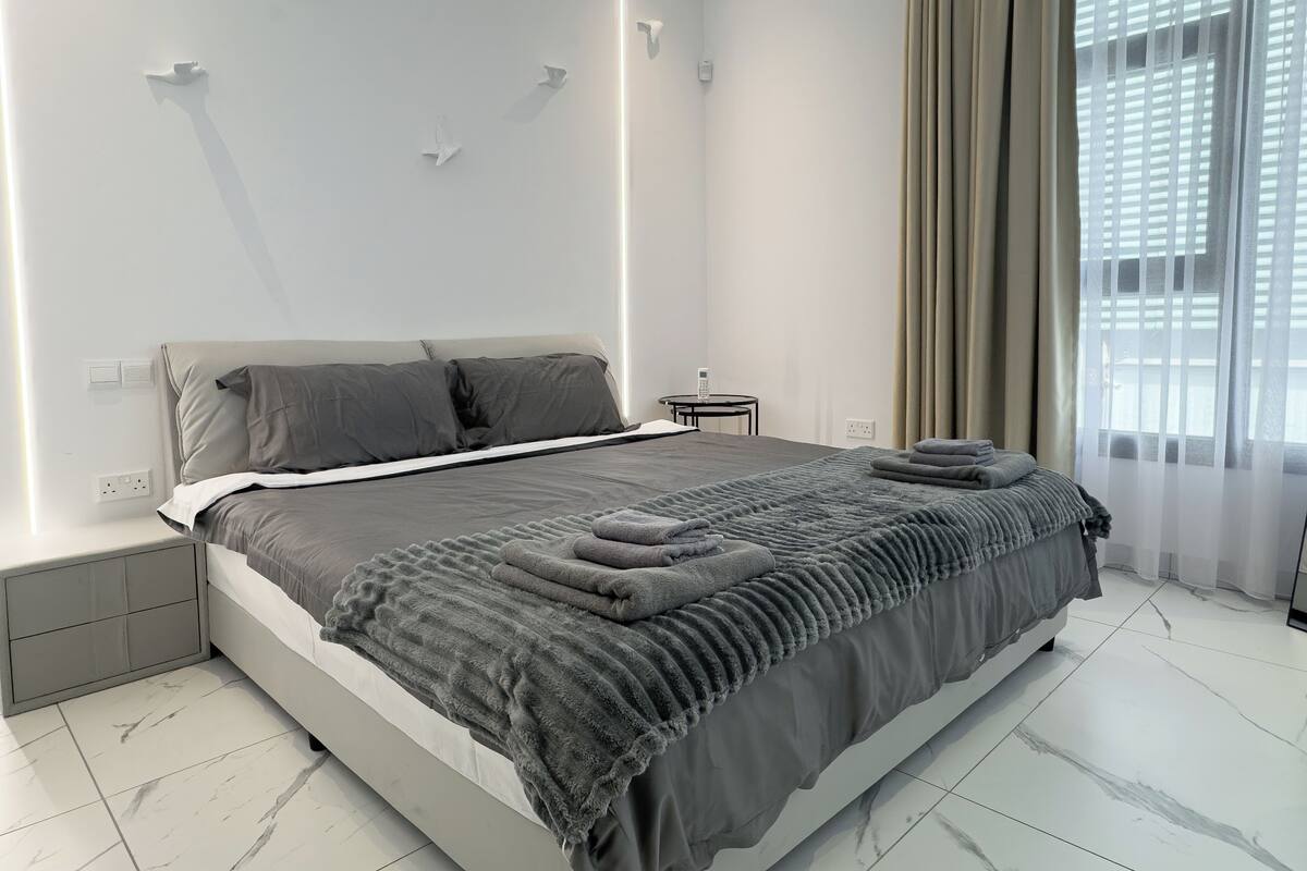 Un dormitorio moderno con cama, mesitas de noche, una ventana con cortinas e iluminación empotrada en la pared.