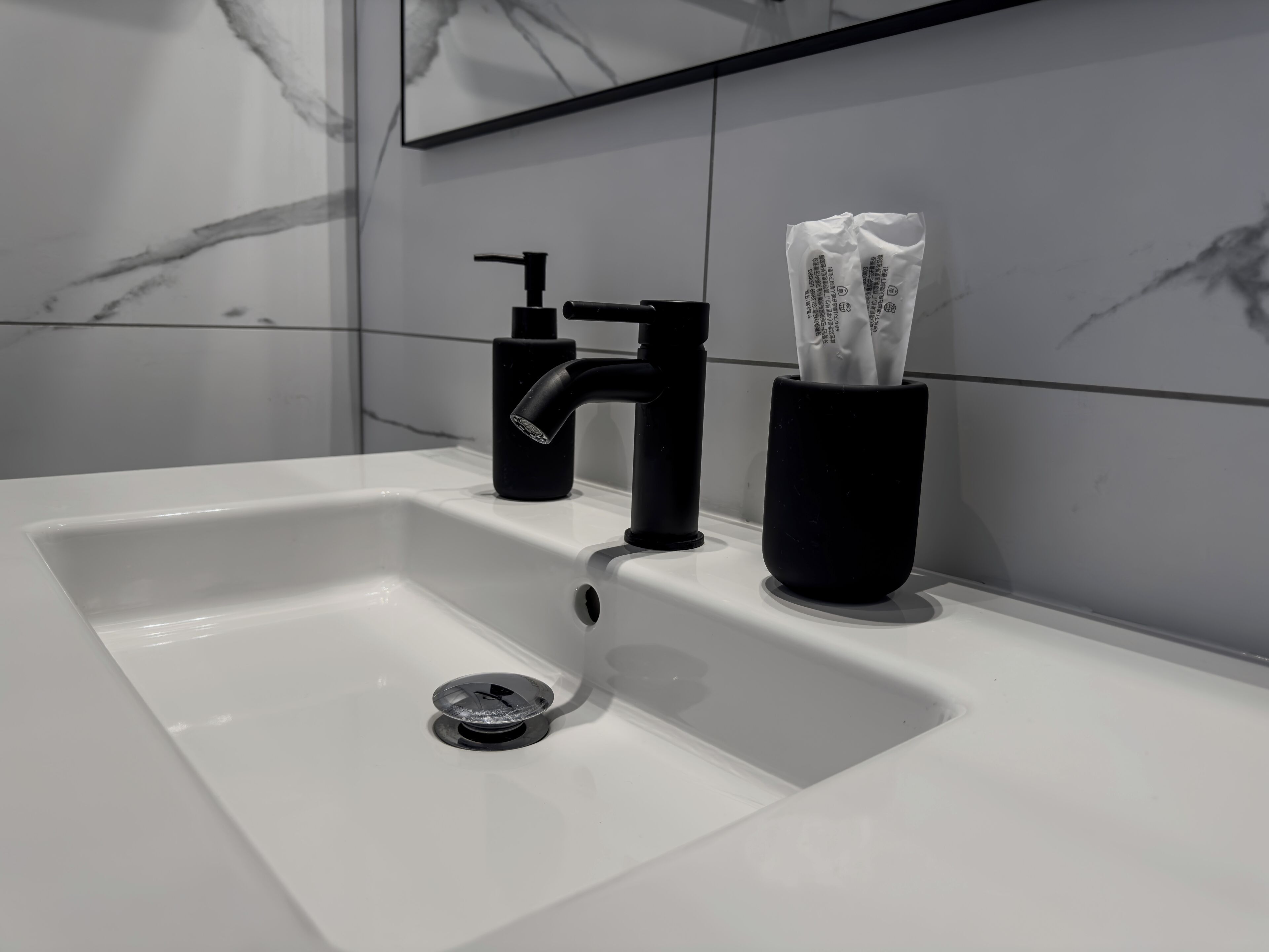 Un baño moderno con un lavamanos blanco, grifo negro y dispensador de jabón.