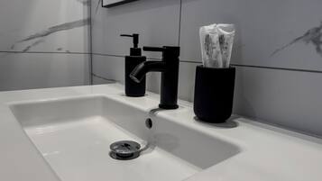 Un baño moderno con un lavamanos blanco, grifo negro y dispensador de jabón.
