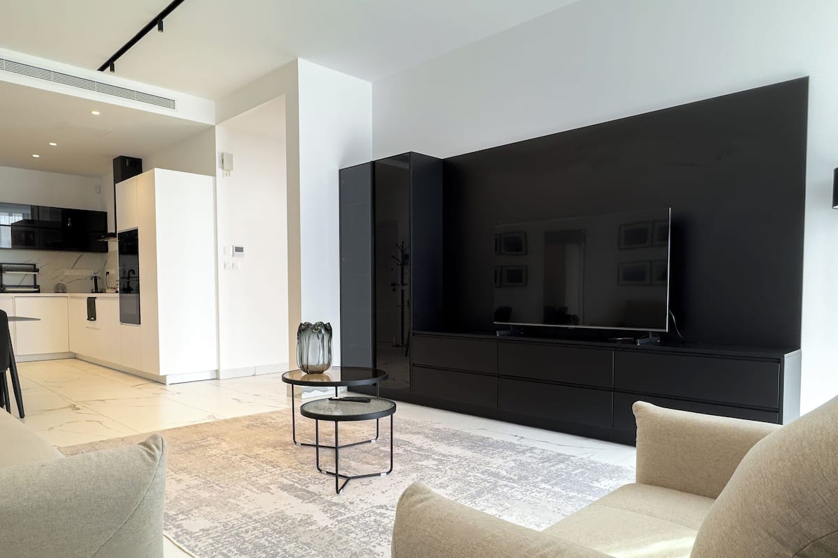 Una sala de estar moderna con un televisor de pantalla plana grande, un sofá, una mesa de centro y una cocina al fondo.