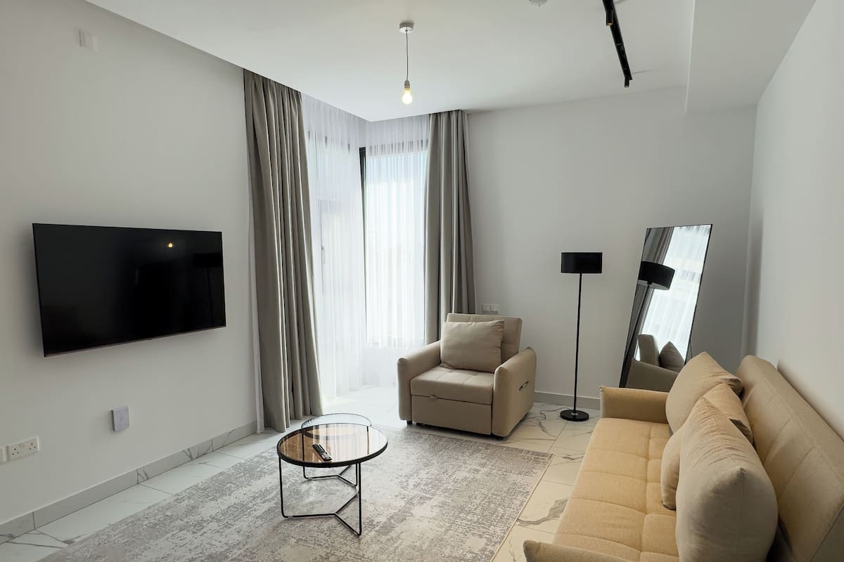 Una sala de estar moderna con una televisión de pantalla plana, una mesa de centro redonda, un sofá, un sillón y una lámpara de pie.