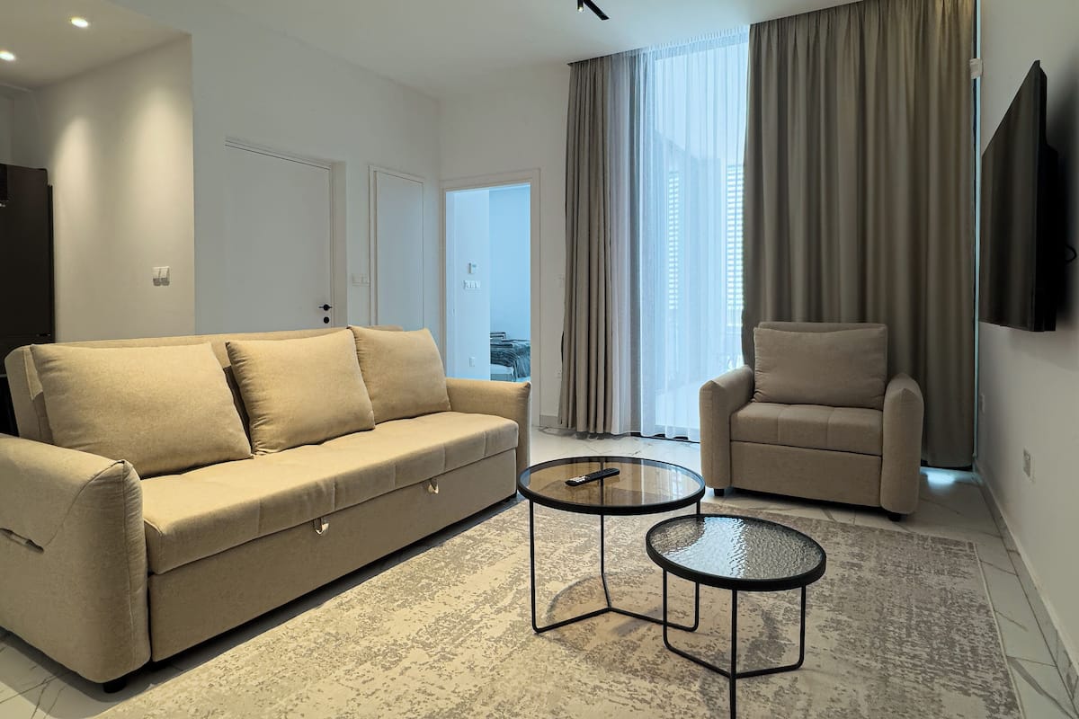 Una sala de estar moderna con sofá, sillón y dos mesas de centro de vidrio.