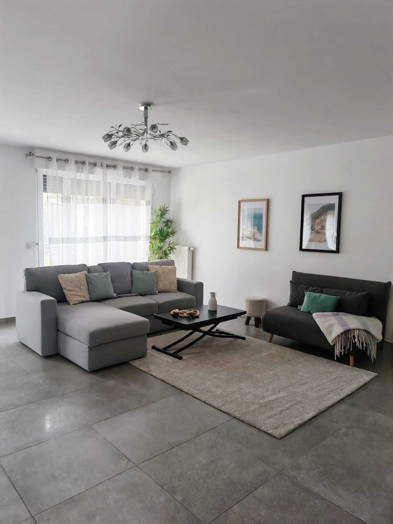 Un salon moderne avec un canapé d’angle, une table basse et un lustre.