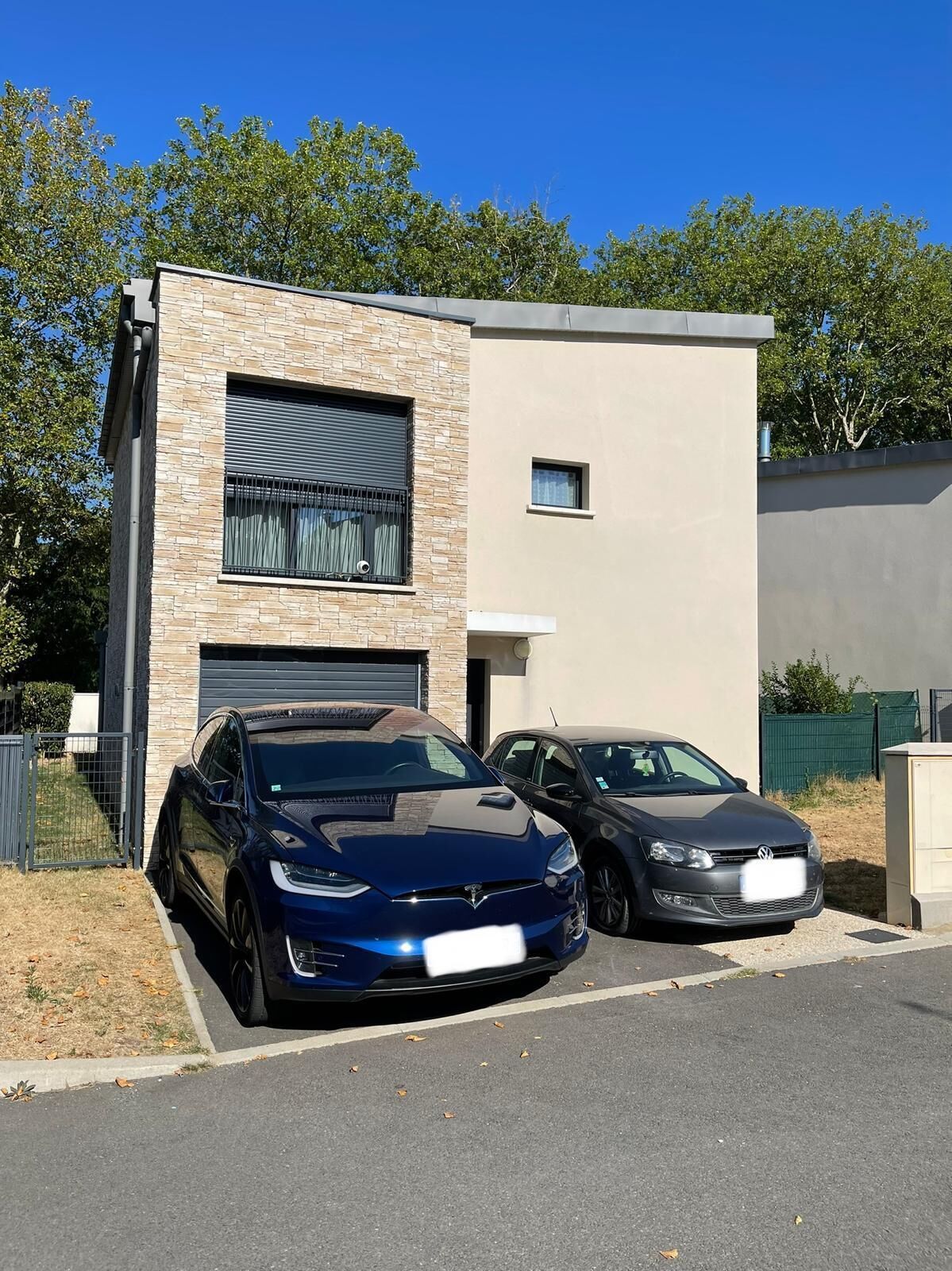 En moderne bygning med garage, to parkerede biler og en klar blå himmel.