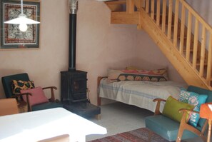 A cozy room with a bed, a wooden chair, a table, a fireplace, and a staircase.