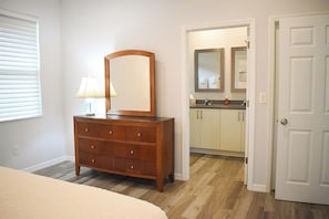A bedroom with a wooden dresser, a mirror, a bedside lamp, and a door leading to a bathroom. - Superb 2-bedroom house with AC in sunny Sarasota (Sarasota)