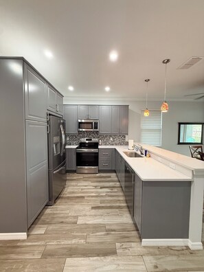 A modern kitchen with grey cabinetry, stainless steel appliances, a herringbone wood floor, and pendant lighting. - Superb 2-bedroom house with AC in sunny Sarasota (Sarasota)