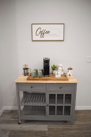 Eine Küchenzeile mit einer Kaffeestation, inklusive Kaffeemaschine, Tassen und einer Teeaufbewahrungsbox.