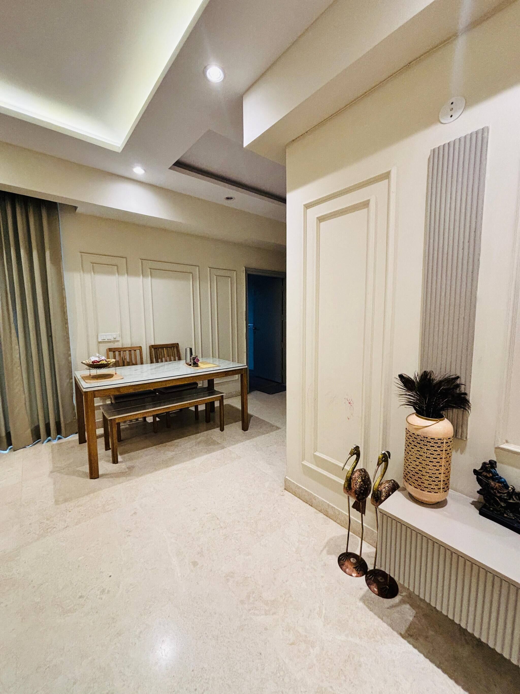 A spacious room with a dining table, chairs, a decorative vase, and a wall-mounted shelf.