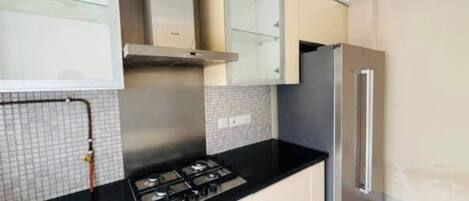 A kitchen with a gas stove, cabinets, a refrigerator, and tiled backsplash.