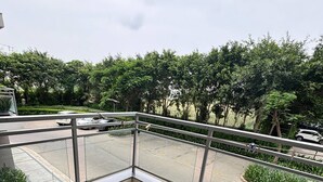 Ein Balkon mit Holztisch und -stühlen, einem Glasgeländer und Blick auf eine Straße mit Autos und Bäumen.