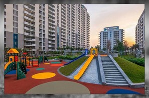 A playground with slides and climbing structures, surrounded by high-rise residential buildings. - Luxurious 2-bedroom Apartment With Shared Pool in Gurugram (Gurugram)