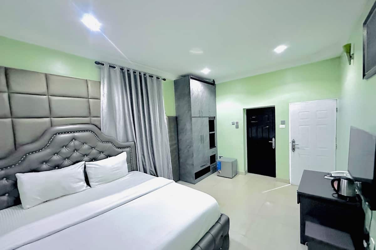 A hotel room with a large bed, a desk with a laptop, a wardrobe, and a door leading to another room.