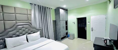 A hotel room with a large bed, a desk with a laptop, a wardrobe, and a door leading to another room.