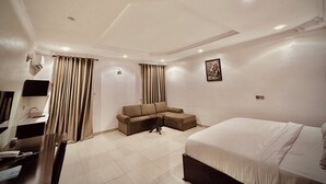 A hotel room with a bed, a sofa, a desk, and a TV. - Nestvier apartment (Abuja)