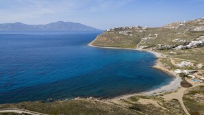 A coastal landscape with a beach, clear blue sea, and scattered buildings on a hillside. - Beach House Houlakia Mykonos (Mykonos)
