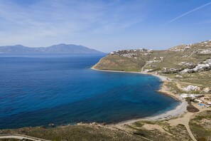 A coastal landscape with a beach, clear blue sea, and scattered buildings on a hillside. - Beach House Houlakia Mykonos (Mykonos)
