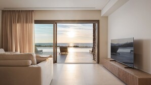 A modern living room with a large TV, a sofa, and a view of the sea through a glass door. - Beach House Houlakia Mykonos (Mykonos)