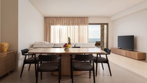 A modern living room with a dining table, chairs, a TV, and a view of the sea. - Beach House Houlakia Mykonos (Mykonos)
