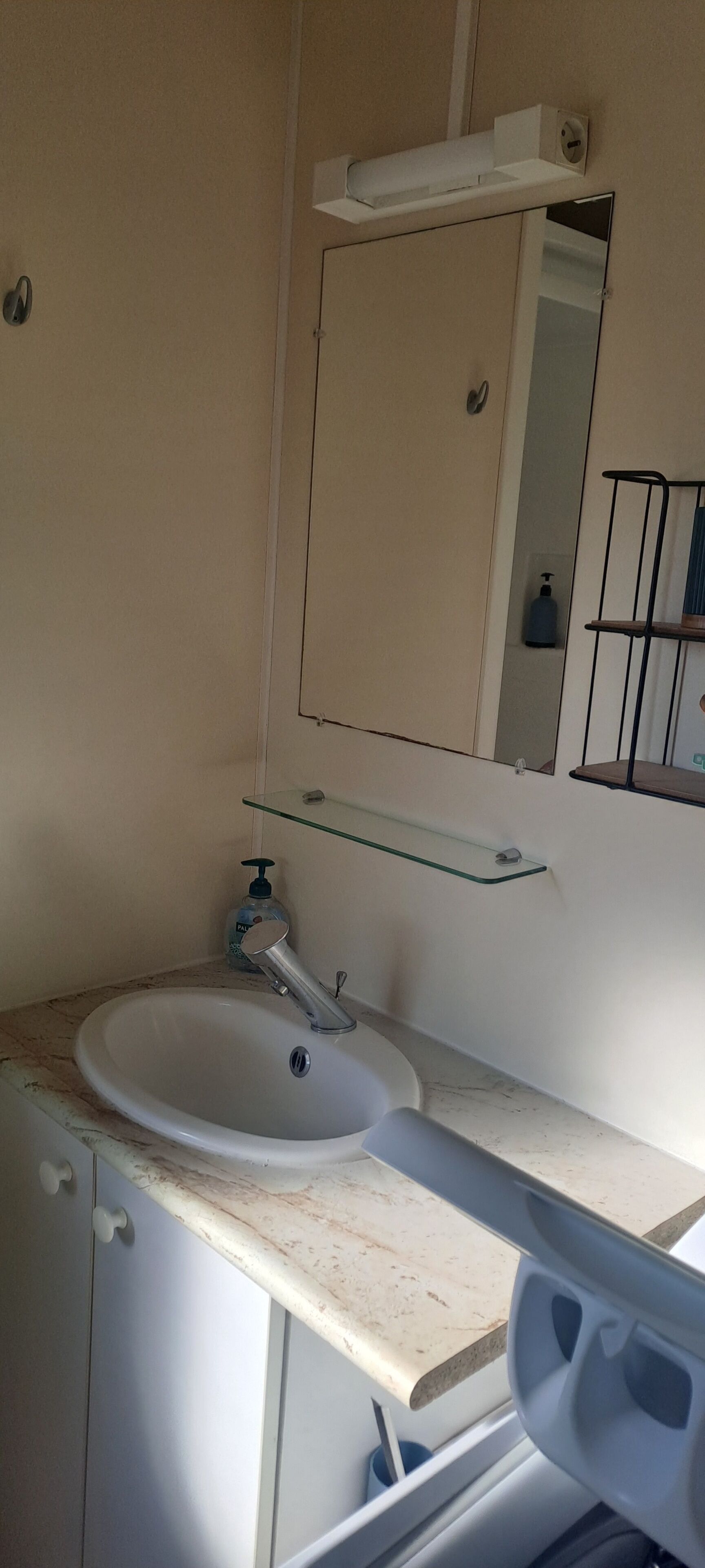 Een badkamer met een witte wastafel, een spiegel en een glazen plank.