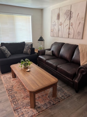 A living room with a dark brown leather sofa, a wooden coffee table, and a patterned rug.