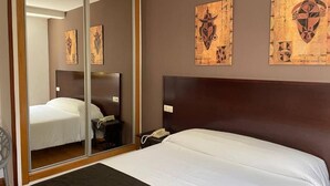 Une chambre d’hôtel avec un lit, une table de chevet avec un téléphone, un miroir et des œuvres d’art accrochées au mur.