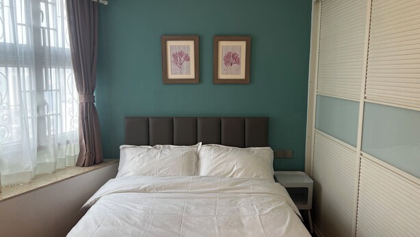Una cama con ropa blanca, un cabecero oscuro y dos láminas botánicas enmarcadas sobre paredes color turquesa.