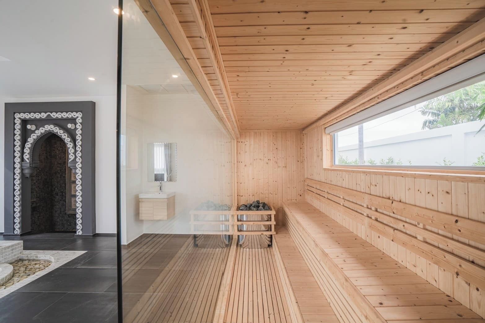 A sauna room with wooden walls and a bench, a sink, and a mirror.