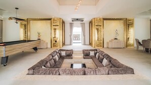 Un vaste espace de vie comprenant une table de billard, un canapé d’angle et un mur décoratif agrémenté de touches dorées.
