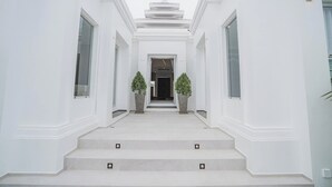 Un bâtiment blanc avec un escalier central menant à une porte, de part et d’autre de laquelle se trouvent des plantes en pot.
