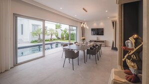 Un espace repas moderne avec vue sur la piscine, une table à manger dressée pour six personnes et une grande fenêtre.