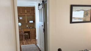 Ein Schlafzimmer mit einem Bett, einer Holztür, einem zur Toilette führenden Flur und einem gerahmten Bild an der Wand.