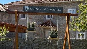 A stone building with a tiled roof, a sign reading 'QUINTA DA LAGINHA,' and a wooden swing set in front.