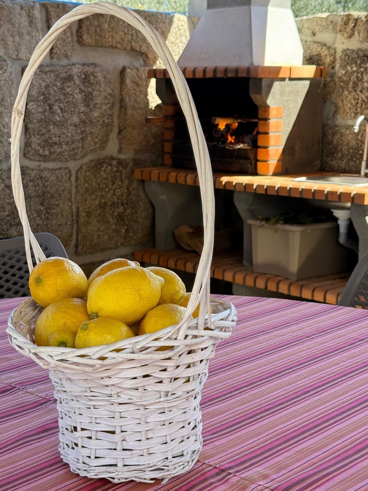 A wicker basket with lemons on a table with a brick oven in the background.