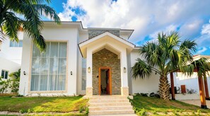 A modern two-story house with a stone facade, large windows, and a well-manicured lawn. - Luxury 4-Bedroom Villa | Puerto Plata | Private Pool & Resort (Puerto Plata)