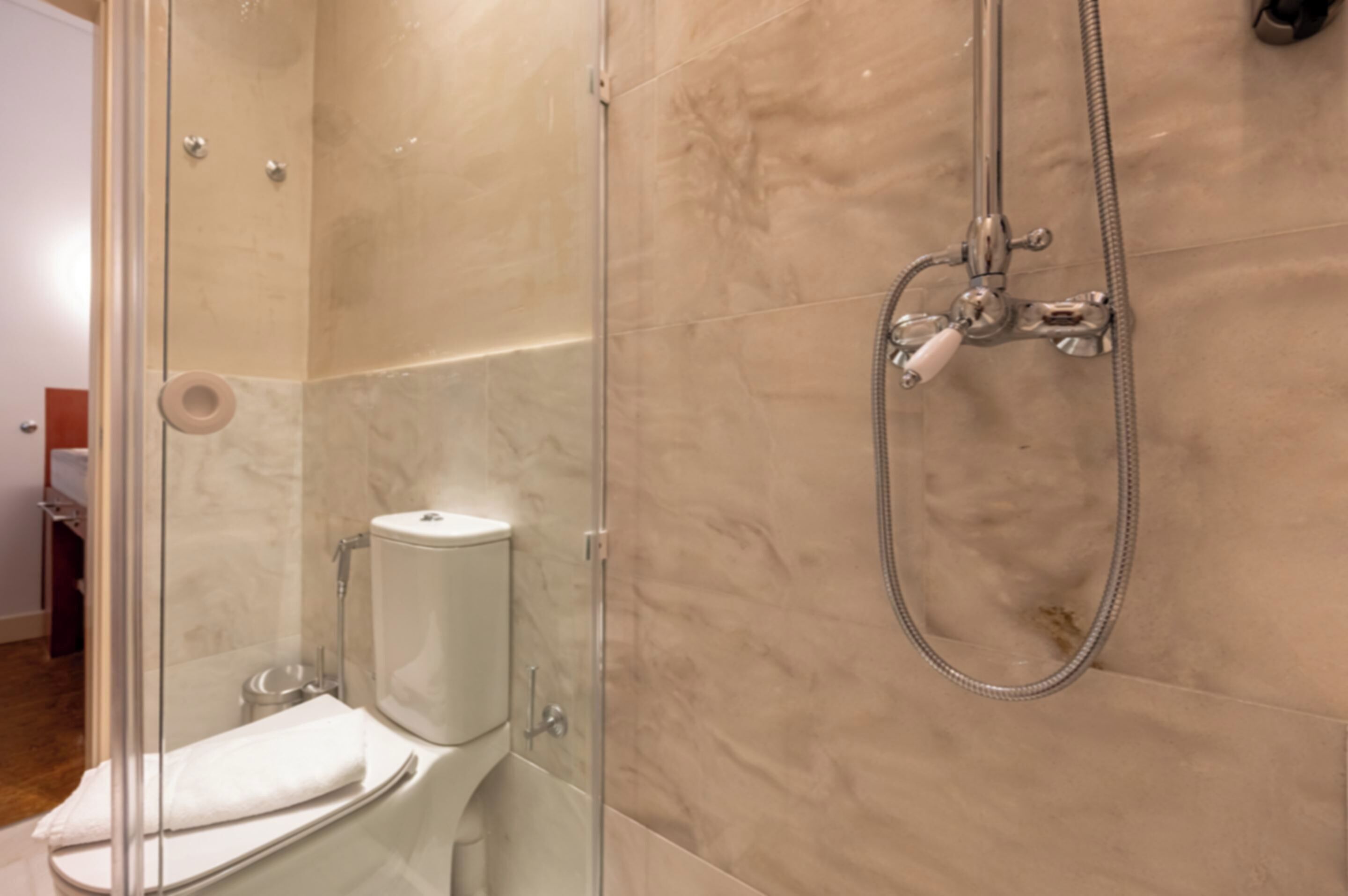 Un baño con ducha envuelta en vidrio, inodoro y pared con azulejos de mármol.
