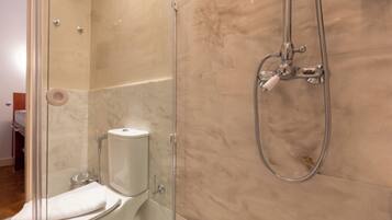 Un baño con ducha envuelta en vidrio, inodoro y pared con azulejos de mármol.
