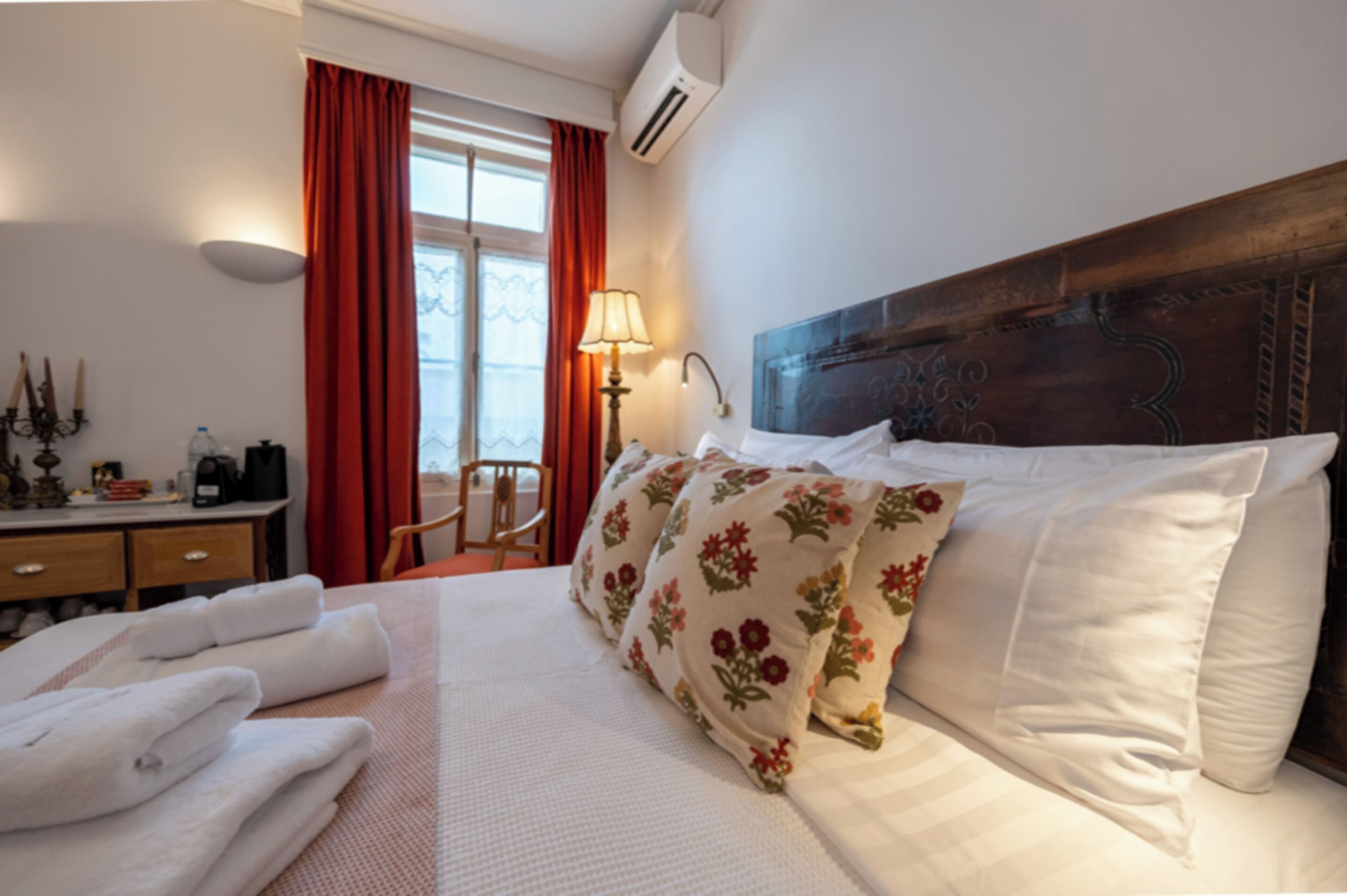 Et hotelværelse med seng, skrivebord, stol, et vindue med gardiner og en aircondition.