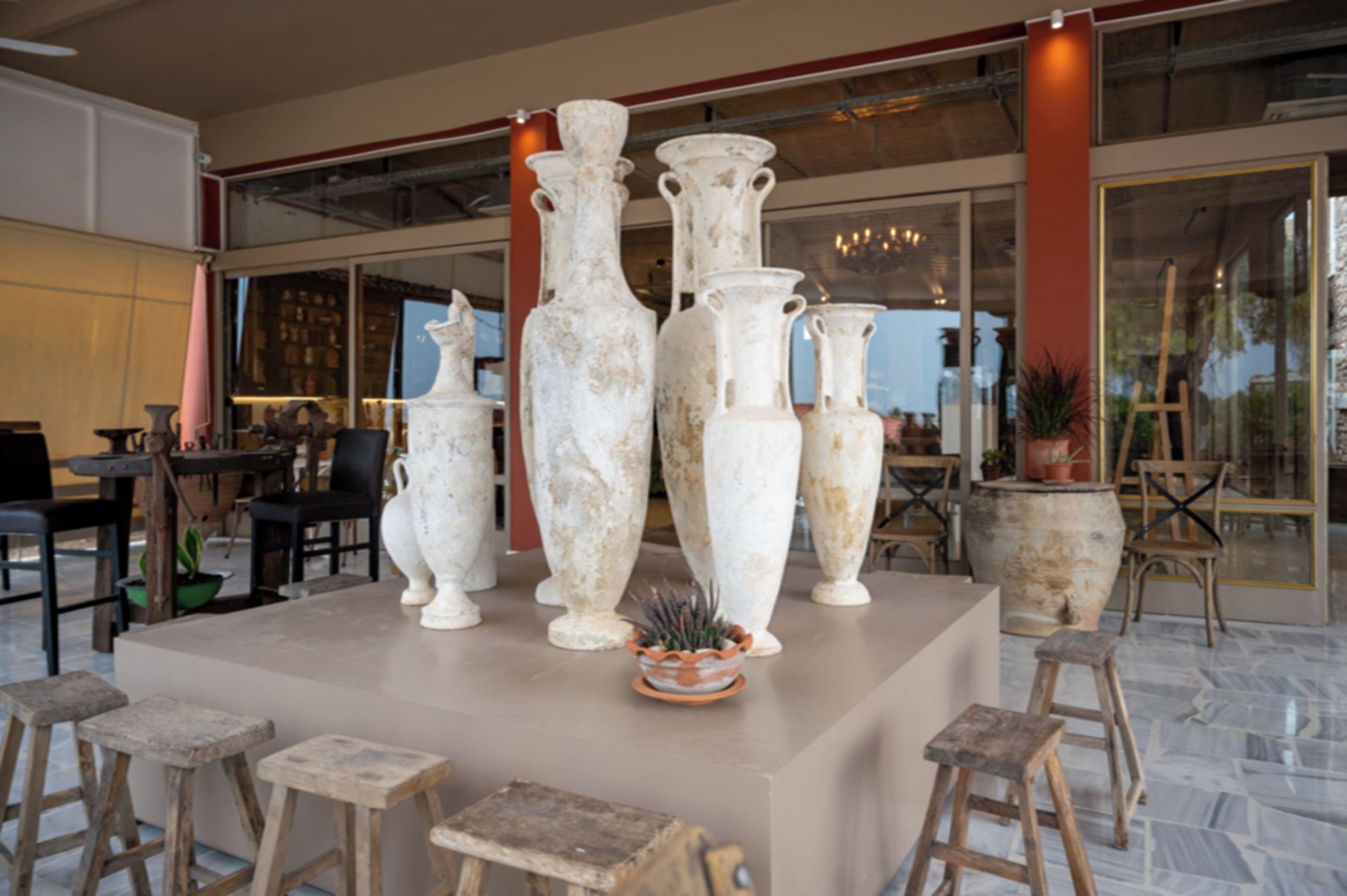 Un área de recepción con una exhibición central de jarrones blancos, arreglos de asientos y un ventanal que ofrece vistas al exterior.