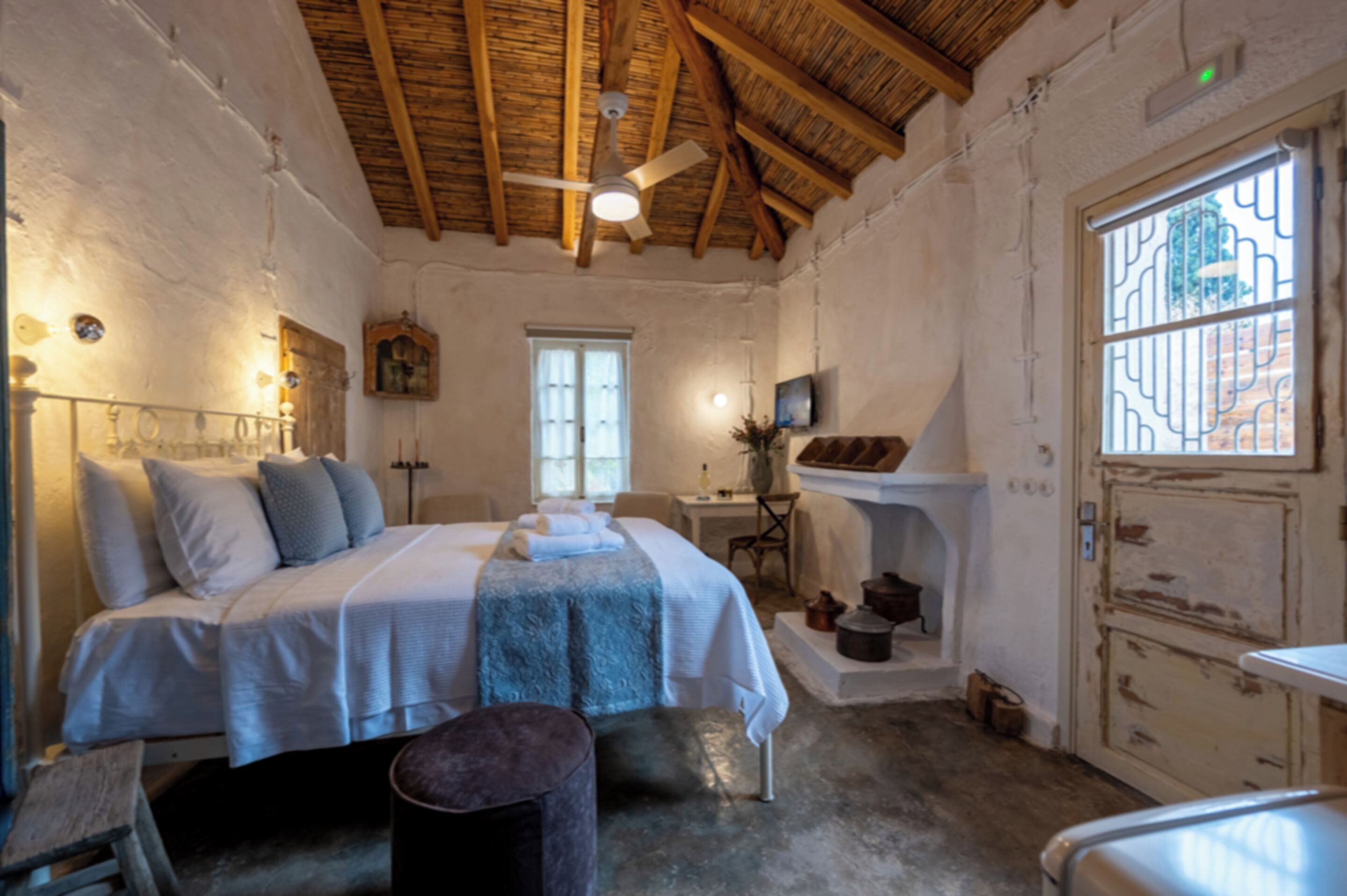 A bedroom with a bed, a desk, a chair, a window, and a ceiling fan.