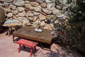 A rustic outdoor seating area with a wooden table and bench, a stone wall, and a small decorative item on the table. - La Belle Hélène de Ménélas 1862 (Mykines)