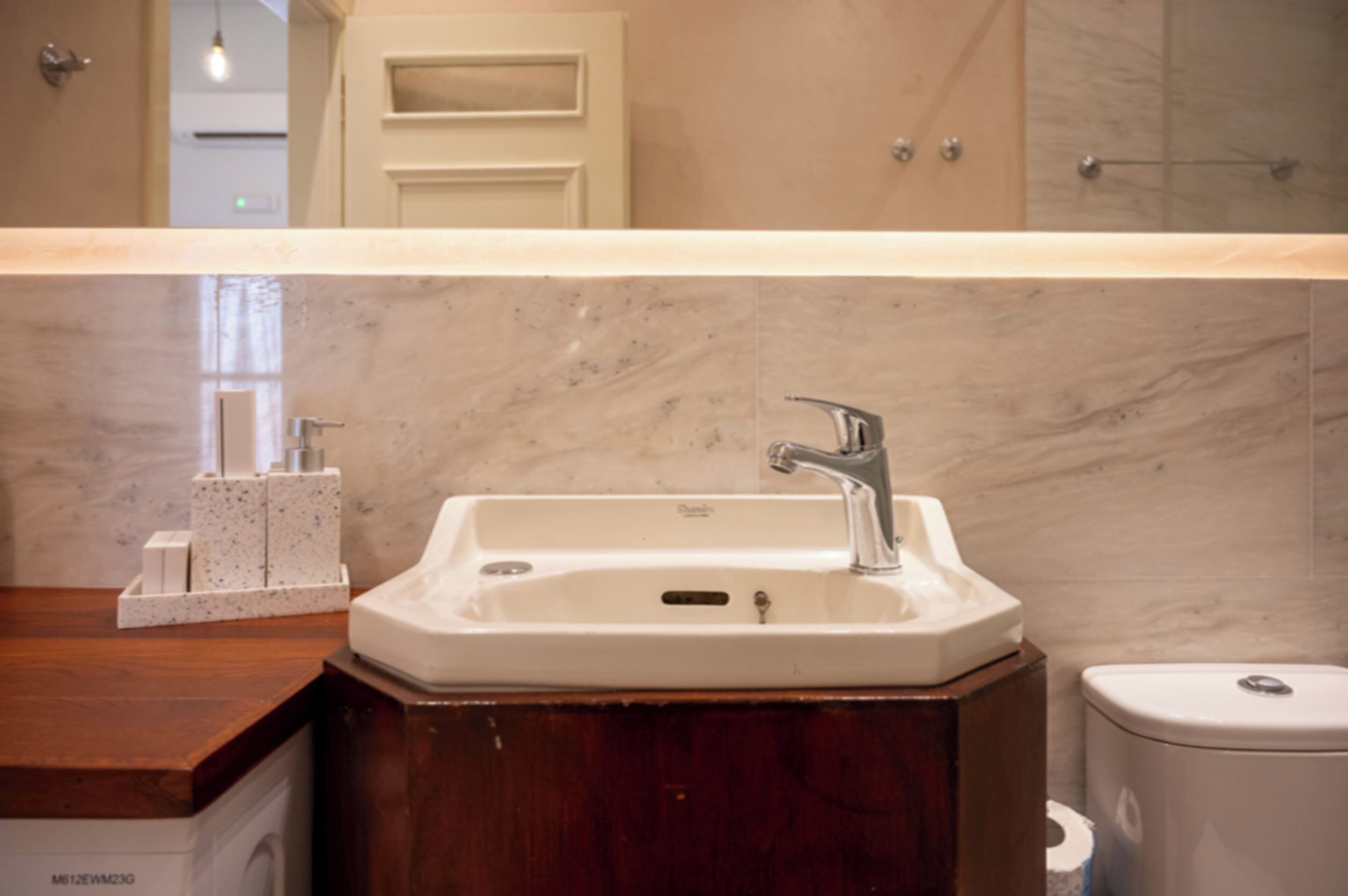 Un baño con lavamanos de mármol, tocador de madera y un inodoro.