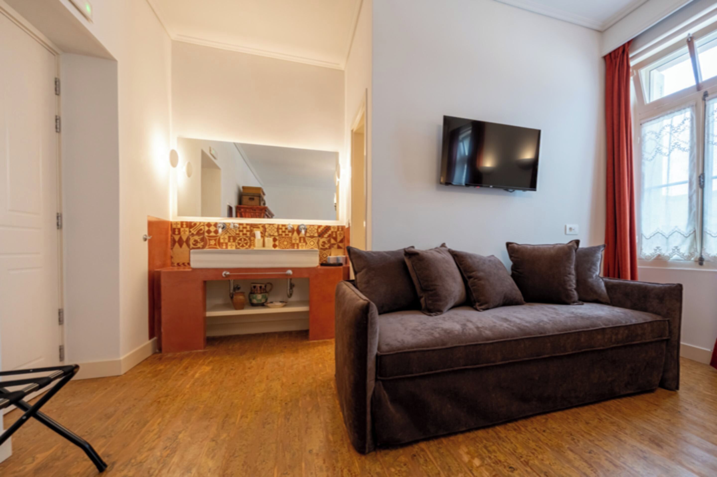 A modern living room with a brown sofa, a flat-screen TV mounted on the wall, and a wooden floor.