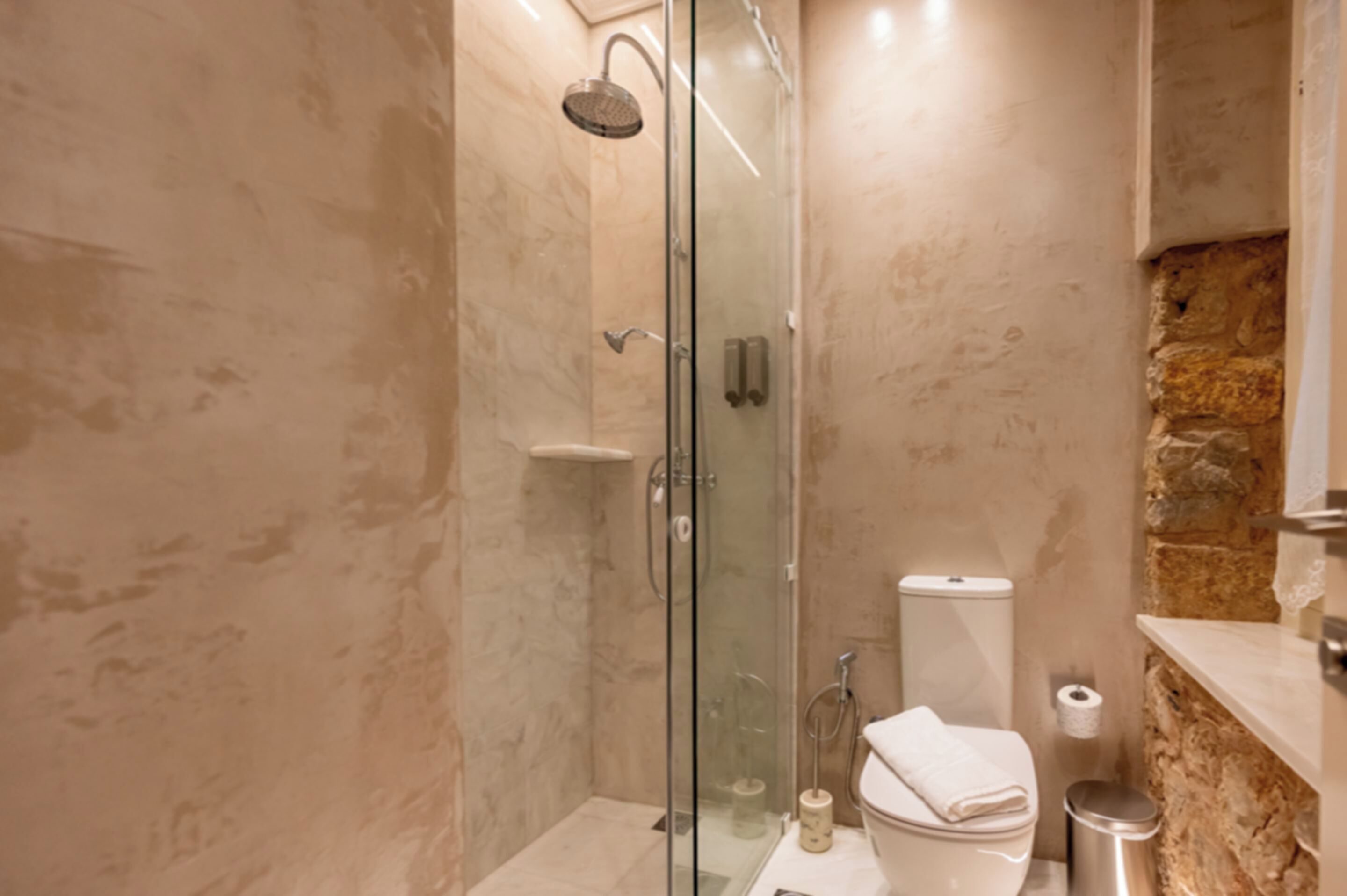 A modern bathroom with a glass-enclosed shower, a toilet, and a marble-tiled wall.