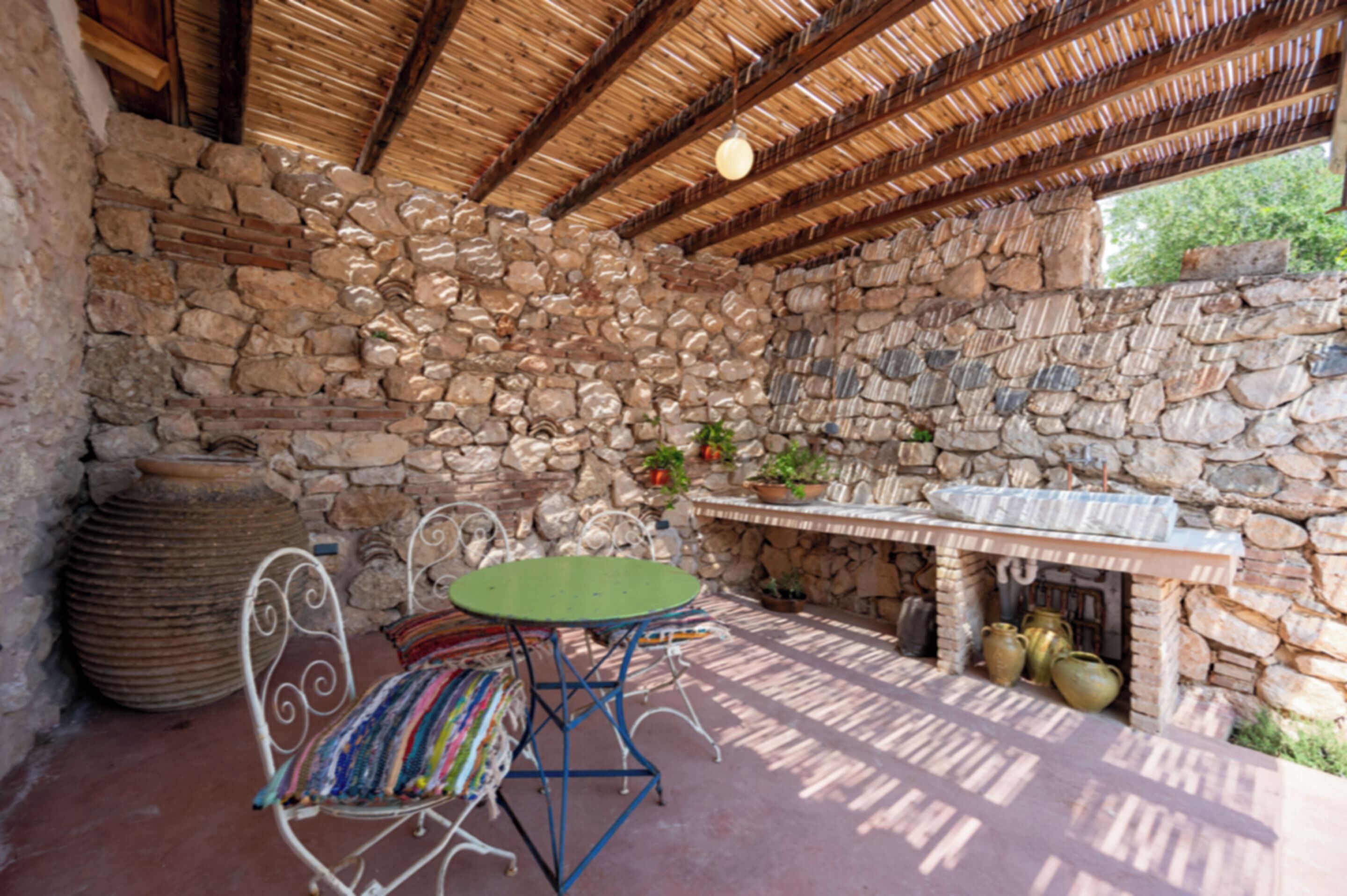 A stone-walled room with a thatched roof, a fireplace, and a table with chairs.