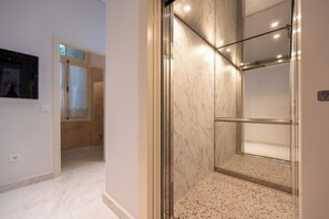 A modern bathroom with a glass shower enclosure, marble walls, and a tiled floor. - La Belle Hélène de Ménélas 1862 (Mykines)