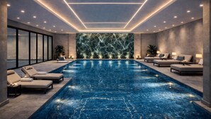 A modern indoor pool with a geometric ceiling design, lounge areas, and a marble wall. - World Star Beach Resort & Spa (Alanya)