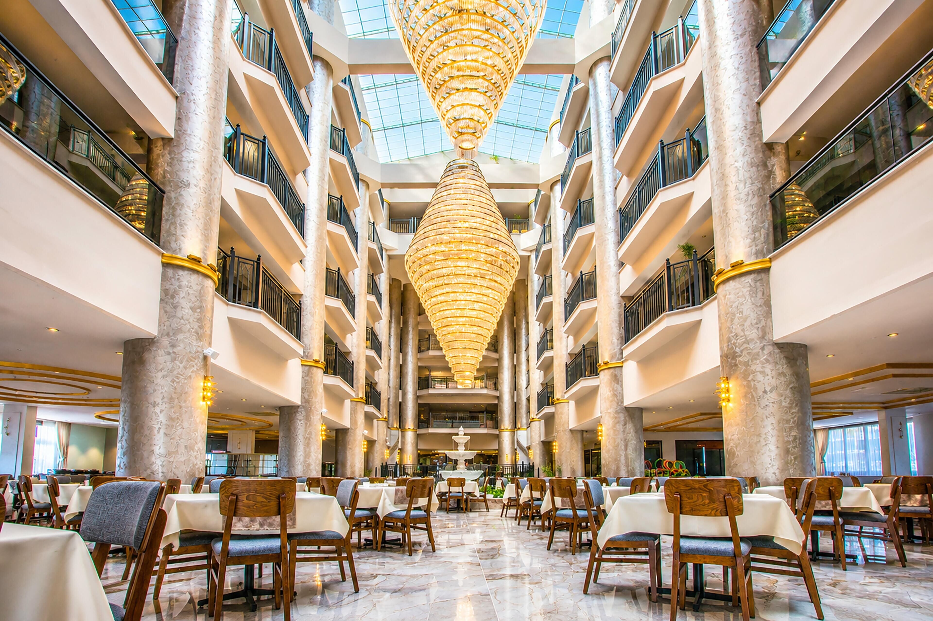 A multi-level atrium with marble columns, a central chandelier, and dining areas with tables and chairs.