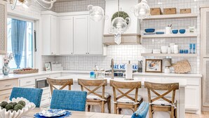 A modern kitchen with white cabinetry, a central island, and blue chairs. - Luxury Pistache Park Retreat | Private Pool + Hot Tub | Carlton Landing (Carlton Landing)