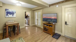Un salón con televisor, muebles de madera, una cocina al fondo y una puerta.